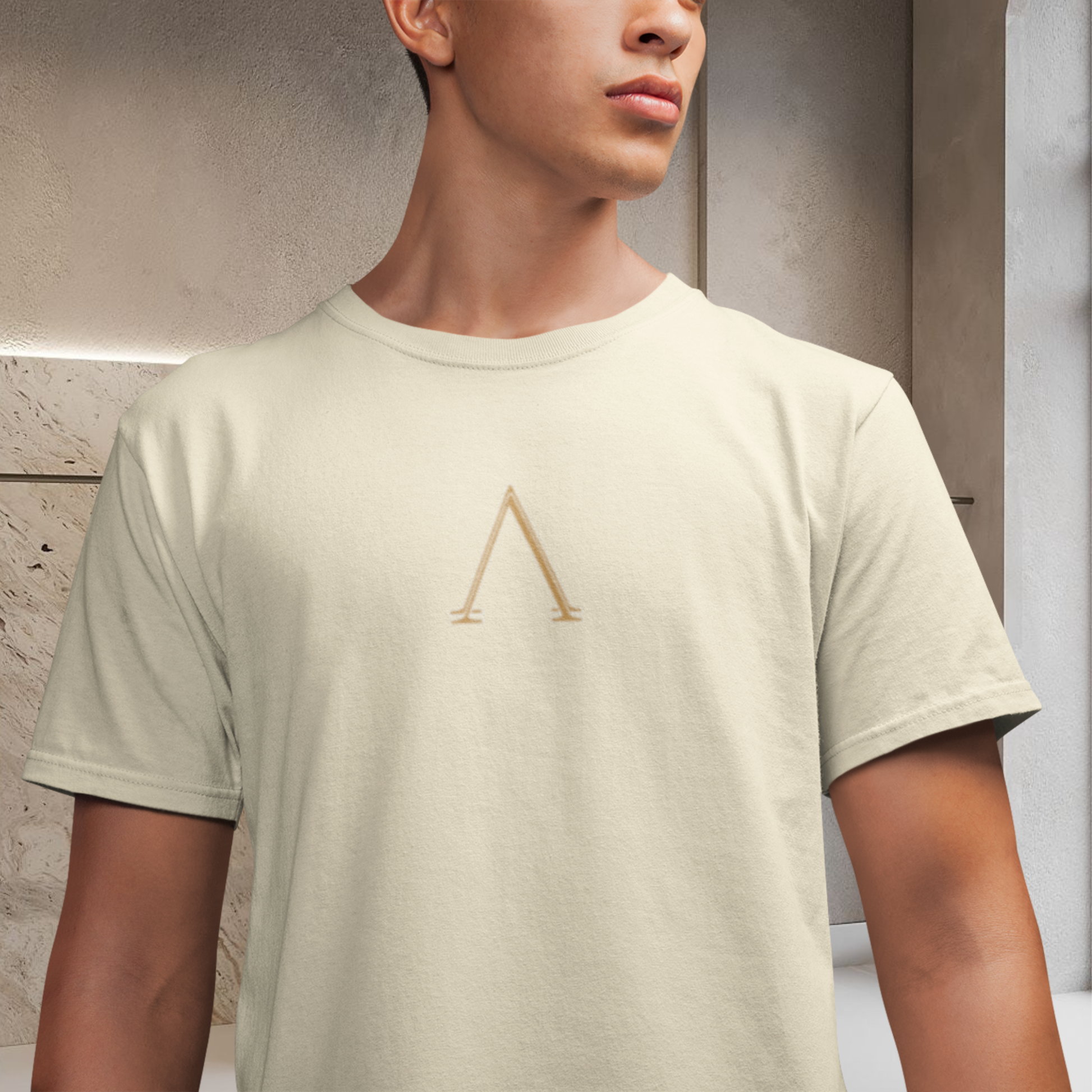 presentation of a white cream color t-shirt 100% cotton wore by a male model face cutted lower body cutted a minimalist symbol on the chest gold color A shape.  spiritually designed t-shirt high vibrational clothing unisex fashion style