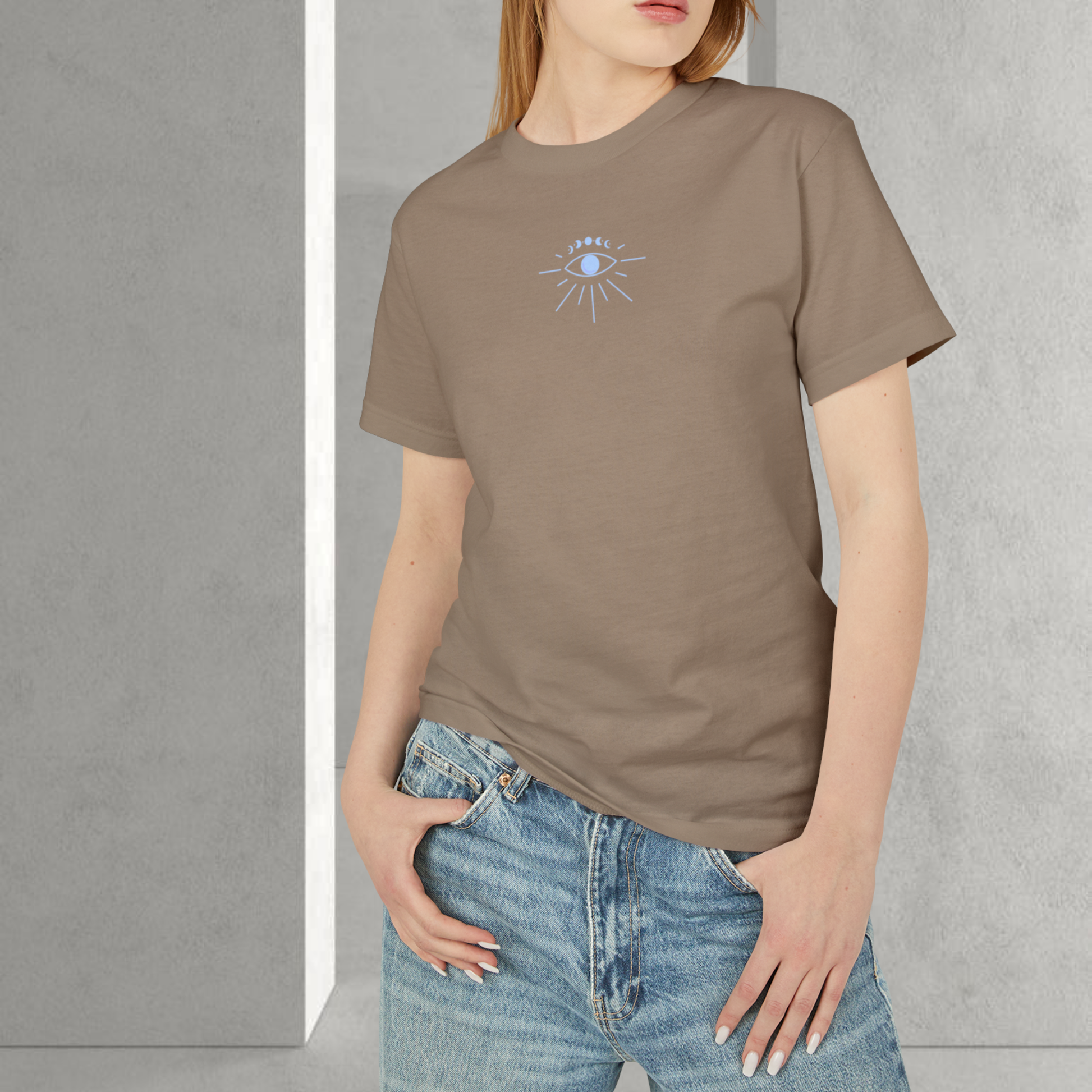 model female wearing a brown t-shirt 100% cotton with a blue silver eye on the chest printed unisex style, she stand on a interior minimalist grey background for spiritually designed brand fashion trendy 