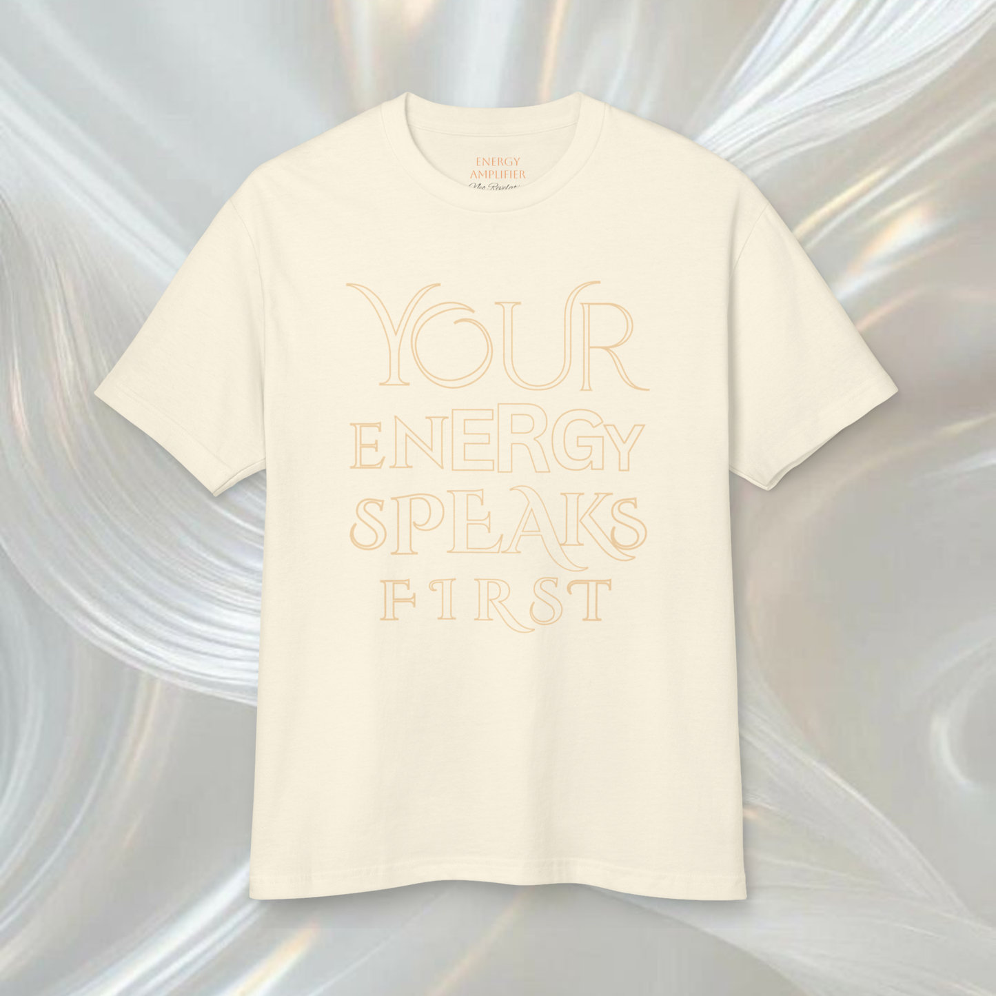 white cream color t-shirt presented on a white ethereal soft background the tee is printed with a quote ' your energy speaks first' in big thin elegant letters this t-shirt si spiritually designed to make it high vibrational a innovative spiritual fashion concept 