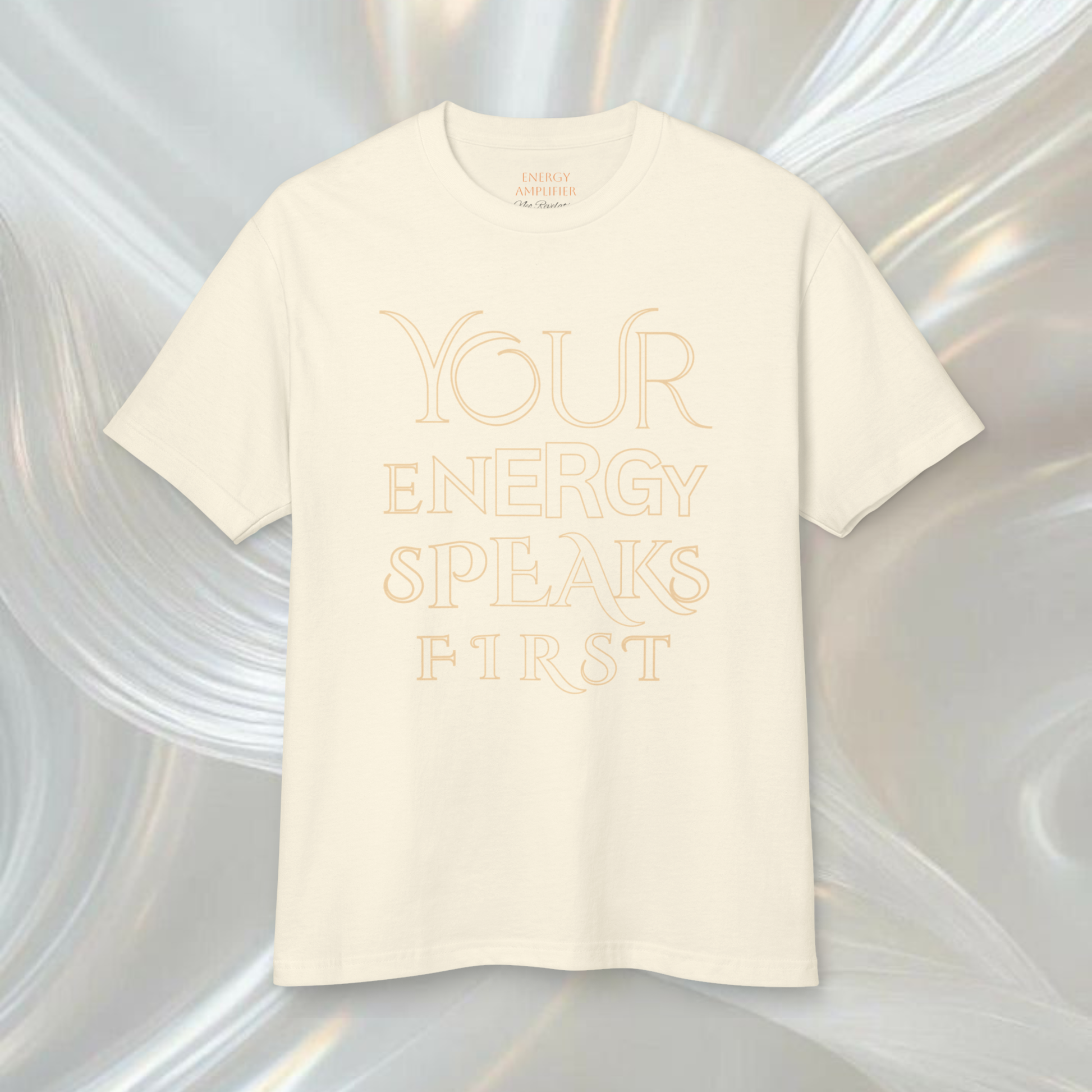 white cream color t-shirt presented on a white ethereal soft background the tee is printed with a quote ' your energy speaks first' in big thin elegant letters this t-shirt si spiritually designed to make it high vibrational a innovative spiritual fashion concept 