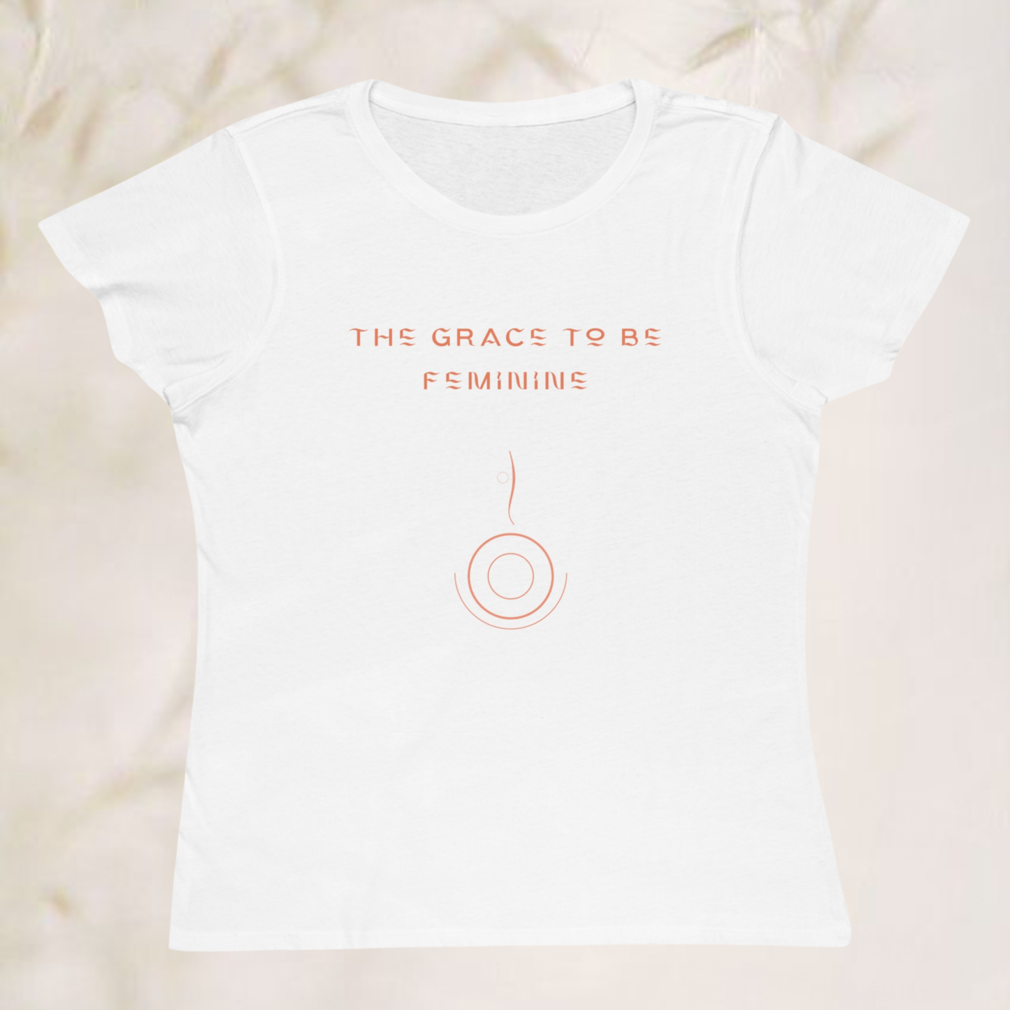 organic cotton t-shirt white color with a minimalist saying 'the grace to be feminine' with a simple symbol the graphic is orange and the background is cream beige color t-shirt 2026 for women from 30 to 70 adults