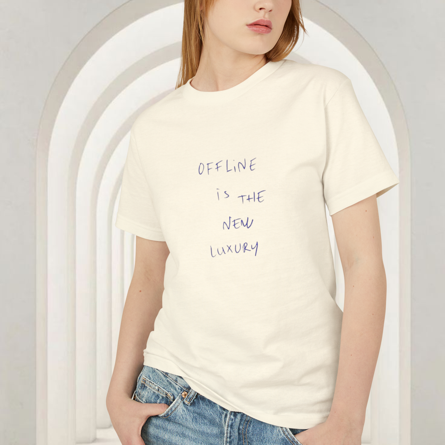 t-shirt cotton faded cream with the quote 'offline is the new luxury' wore by a red head female model european style wearing a jean  and the t-shirt with the hand written saying 'offline is the new luxury' in black color