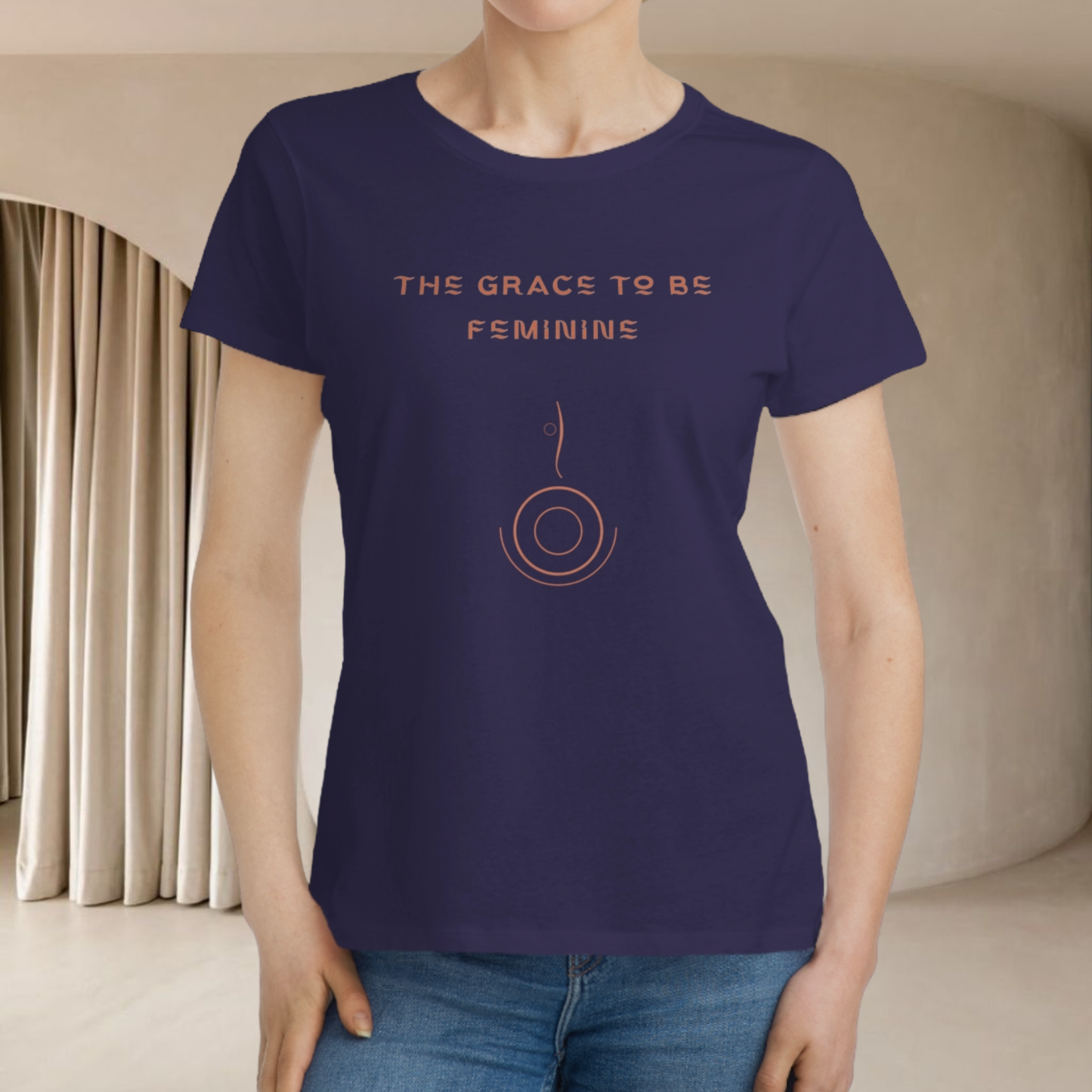 spiritual t-shirt purple dark with the saying 'the grace to be feminine' in orange with a minimalist symbol of feminine grace round shape with a line going up, the model is european white type we don't see her face she stand in interior minimalist beige background